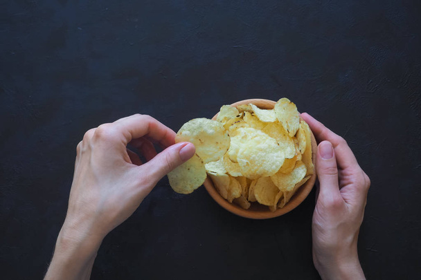 Женские руки держат вкусные картофельные чипсы на темном фоне
. - Фото, изображение