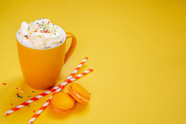 Close up of yellow coffee cup, straws and french macaroons over yellow background. - Foto, imagen
