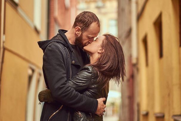 Atraktivní pár, vousatý muž a bruneta dívka líbání mimo staré Evropské ulice na pozadí. - Fotografie, Obrázek