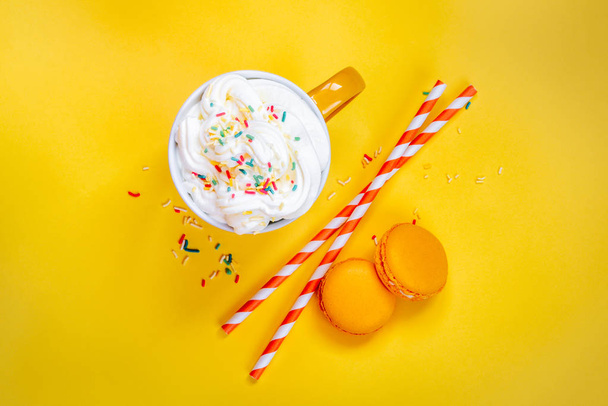 Top view of yellow coffee cup, straws and french macaroons over yellow background. - Foto, afbeelding