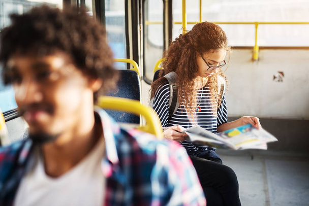 Young adorable woman with curly hair is sitting in a bus and reading newspaper - 写真・画像
