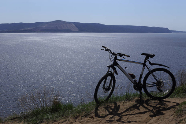 大きな川の背景にスポーツ自転車のシルエット。遠くに山々 があります。青い空 . - 写真・画像