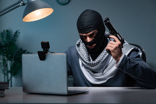 Terrorist burglar with gun working at computer - 写真・画像