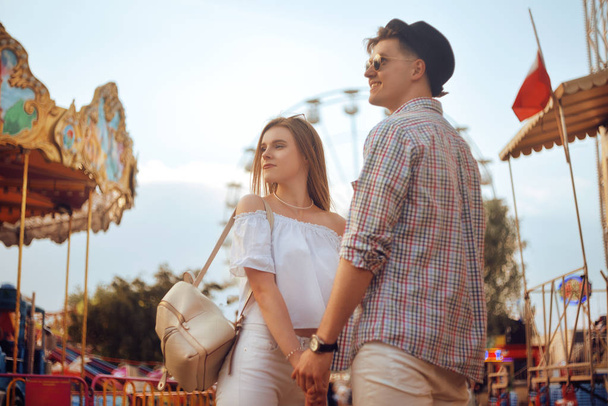 Beautiful, young couple having fun at an amusement park. Couple Dating Relaxation Love Theme Park Concept. Couple posing together on the background of a ferris wheel. Tourists have fun, smile - Photo, Image