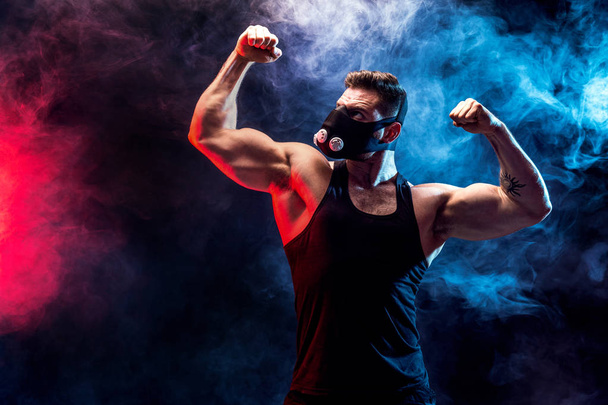 Strong male athlete in a black training mask on a black background - Foto, Bild