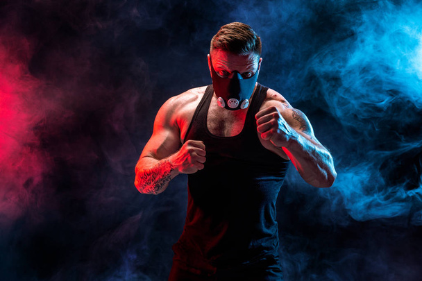 Strong male athlete in a black training mask on a black background - Foto, Imagen