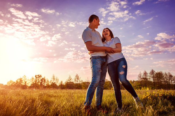 Couple having fun in spring field. Young man and girl hugging and laughing at sunset. - Photo, Image