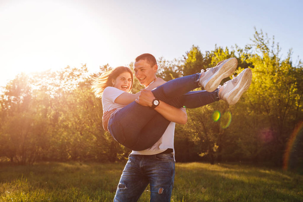 Couple having fun in spring forest. Man holds his girlfriend in hands and spins at sunset. - Foto, Imagen