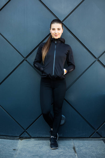 Городской спорт. Портрет молодой красивой фитнес-женщины, изолированной на черной стене улицы
 - Фото, изображение
