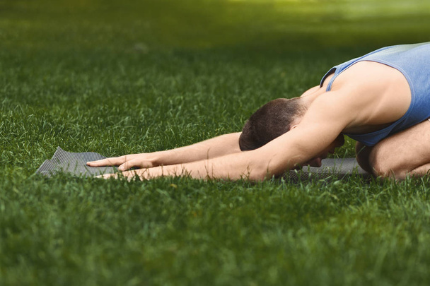 Jonge man opleiding yoga in childs pose buitenshuis - Foto, afbeelding