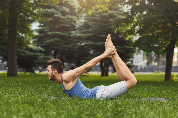 Jonge man opleiding yoga in boog pose buitenshuis - Foto, afbeelding