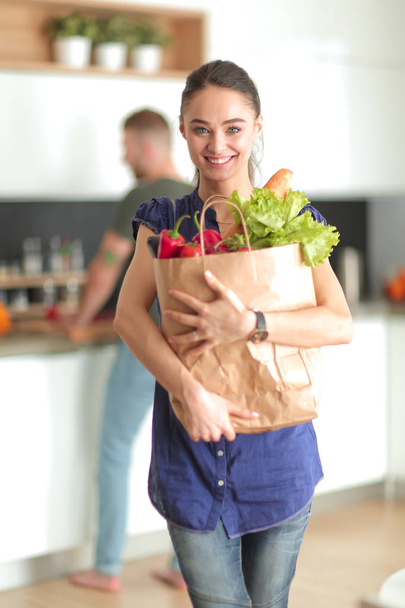 Fiatal pár a konyhában, nő egy zacskó élelmiszerrel bevásárlás - Fotó, kép