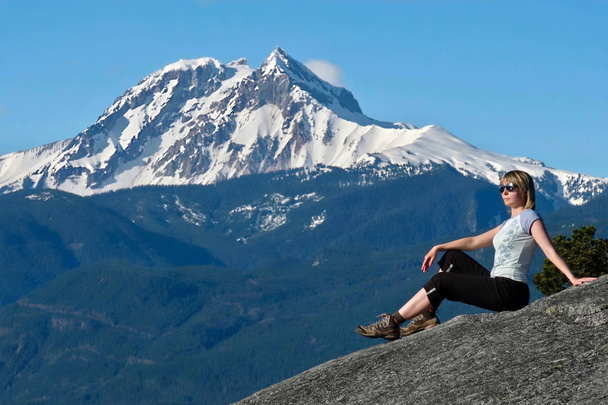 Matkustaa Kanadaan. Nainen vuorella kalliolla lumihuippua vasten
 - Valokuva, kuva
