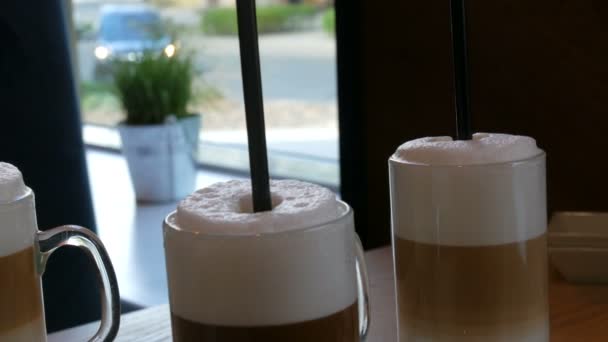 Όμορφη γυαλιά με καφέ latte και μεγάλο αφρού στο καφενείο στο τραπέζι - Πλάνα, βίντεο