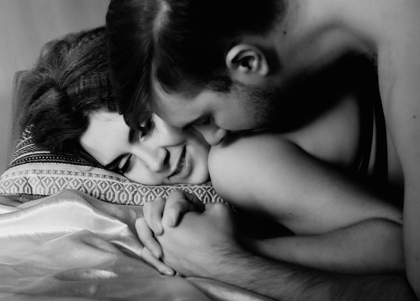 Young beautiful loving couple is embracing on a bed. ntimate image of sensual couple foreplay, kissing passionately. black and white - Foto, imagen
