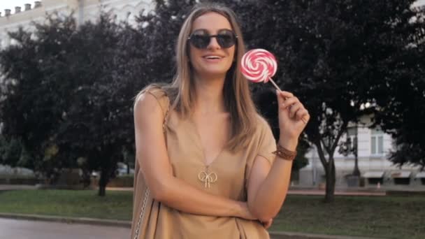 Slow motion video szczęśliwy uśmiechający się kobieta stwarzających w parku z wielki lizak - Materiał filmowy, wideo