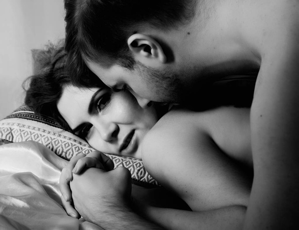 Young beautiful loving couple is embracing on a bed. ntimate image of sensual couple foreplay, kissing passionately. black and white - Foto, Imagen