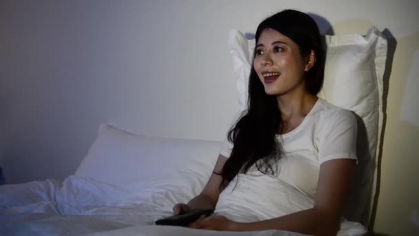Girl watching movie TV laughing having fun in bed. mixed race asian chinese model. - Filmati, video