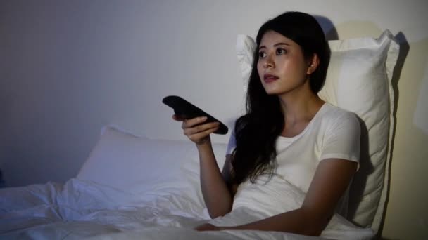young girl sitting on a bed watching a horror movie scary to cove her eyes on TV. mixed race asian chinese model. - Filmmaterial, Video