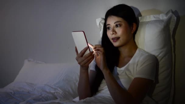 using smartphone message texting working and touch screen at late night sitting on bed. Mobile addict concept. mixed race asian chinese model - Filmagem, Vídeo
