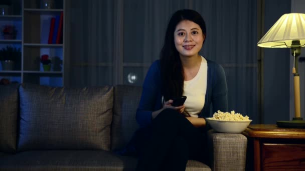 happy attractive lady eating popcorn and selection tv channel searching interesting movie sitting on sofa couch in living room at night. - Video, Çekim
