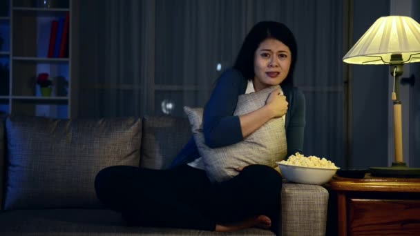 attractive sweet woman sitting on comfortable sofa couch showing afraid emotional with gesture when she watching horror movie at night alone. - Záběry, video