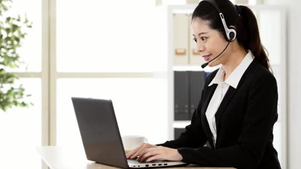 Glimlachend Aziatische vrouw met een hoofdtelefoon en werken op de laptop in kantoor - Video