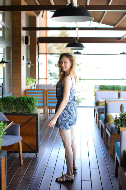 Nuori nainen seisoo kahvilassa lähellä nojatuoleja ja huonekasveja
. - Valokuva, kuva