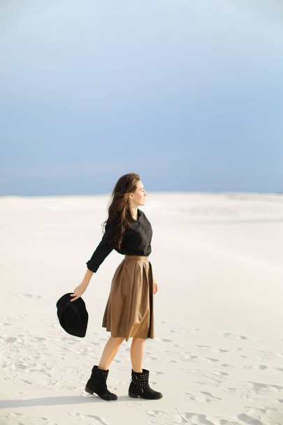 American female photo model standing on snow and wearing skirt and black blouse. keeping hat. - Photo, Image