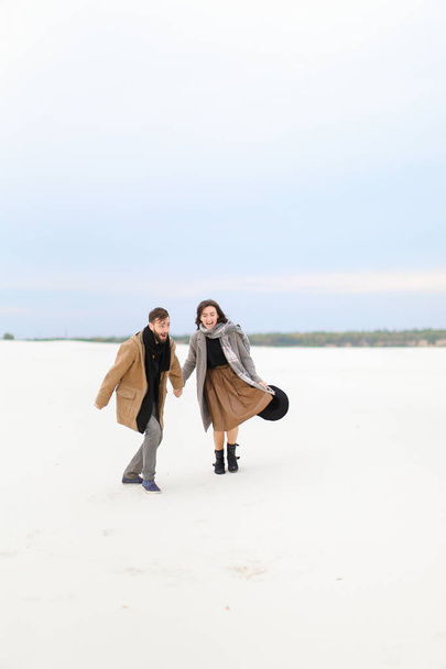 Paltonu ve kaşkolünü giyen adamla karda yürüme ve el, tutan genç mutlu kadın. - Fotoğraf, Görsel