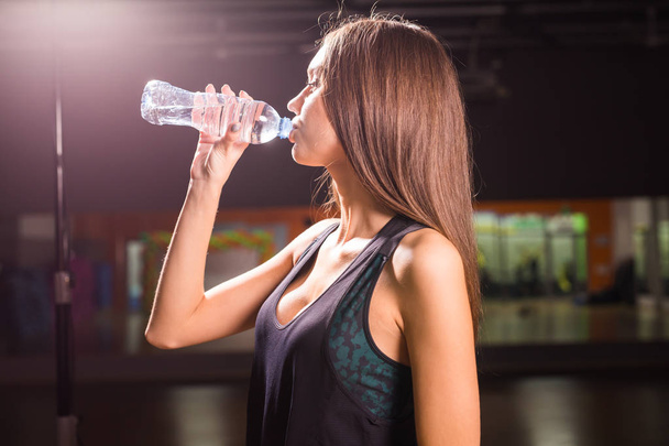 Fitness mladá žena pitnou vodu v tělocvičně. Svalnatý žena pauzu po cvičení - Fotografie, Obrázek