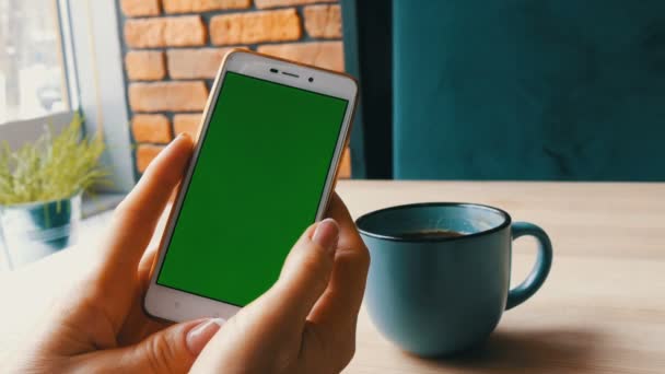 Vihreän ruudun älypuhelin. Chroma Avain valkoiseen älypuhelimeen, naisten kädet pitävät matkapuhelinta kahvilassa kahvin vieressä
 - Materiaali, video