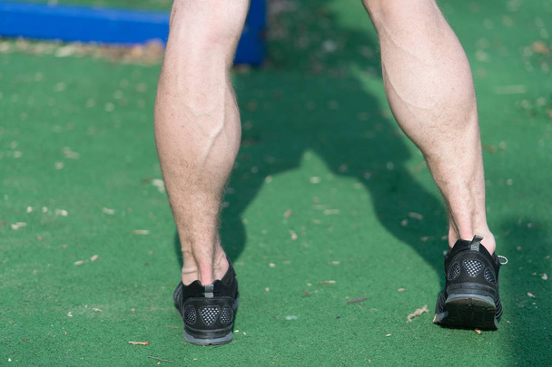 Nogi w czarny sport moda buty na zielonej trawie. Mięśni nóg z żyły na stadion lub arena na słoneczny odkryty. Zdrowia i zdrowego stylu życia. Sport szkolenie i trening - Zdjęcie, obraz