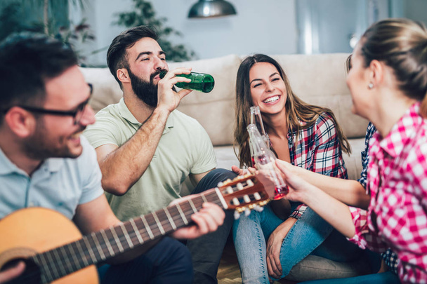 Group of happy young friends having fun and drinking beer in home interior - Foto, Imagem