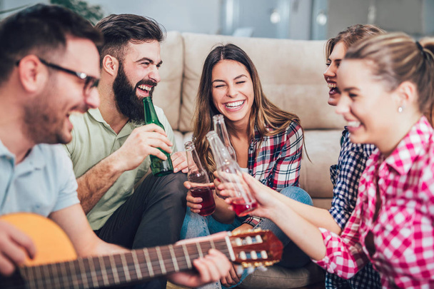 Group of happy young friends having fun and drinking beer in home interior - 写真・画像