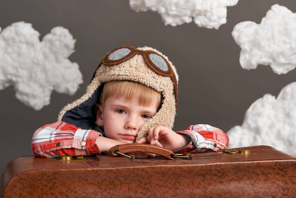 boy dressed as an airplane pilot sit between the clouds with old suitcase and dreams - Foto, afbeelding