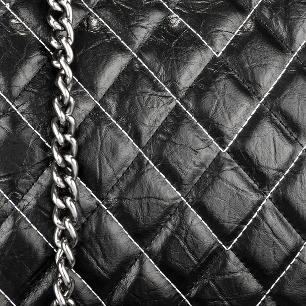 schwarzes Leder strukturiertes Material mit Fäden in Form von Rauten mit einer hängenden Metallkette genäht - Foto, Bild