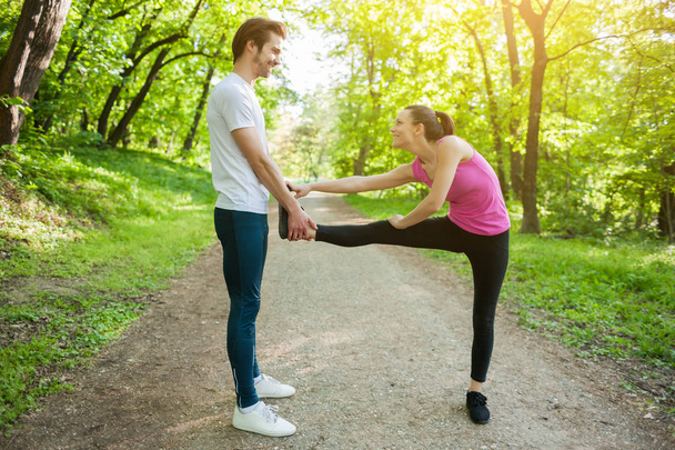 Couple is exercising in park. They are stretching bodies. - Zdjęcie, obraz