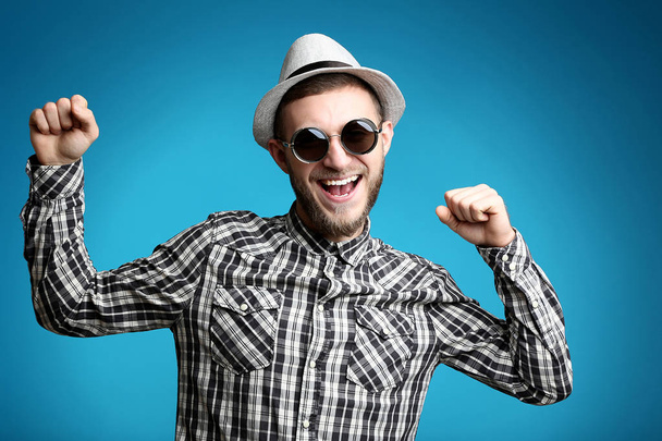 Portrait of young man with sunglasses and hat on blue background - 写真・画像