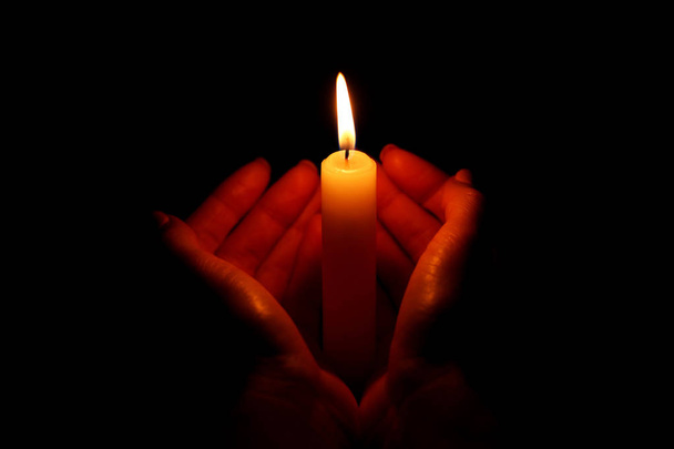 Naisen kädet pitämällä polttava kynttilä mustalla taustalla
 - Valokuva, kuva