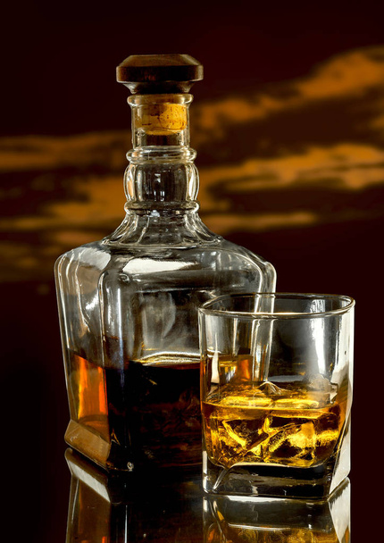 Bottle and glass of whiskey with ice on dark glassy table - Valokuva, kuva