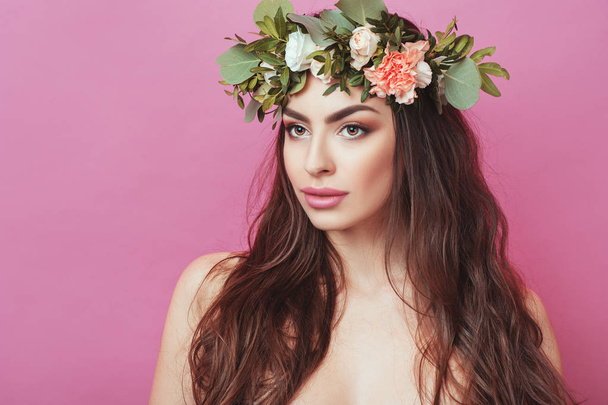 Πορτρέτο του όμορφη νεαρή σεξουαλική αισθησιακή γυναίκα με τέλειο δέρμα κάνει streaming μαλλιά και λουλούδια στο κεφάλι σε ροζ φόντο. Στεφάνι με λουλούδια άνοιξη καλοκαίρι μόδα τρόπο ζωής ανθρώπων έννοιες. - Φωτογραφία, εικόνα