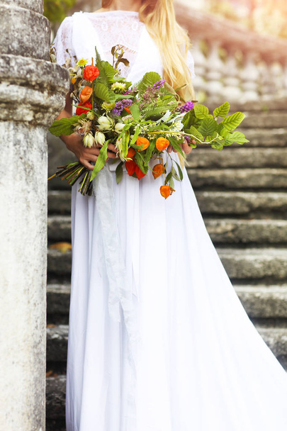 Blonďatá žena s kyticí pózuje ve svatebních šatech. Detailní záběr - Fotografie, Obrázek