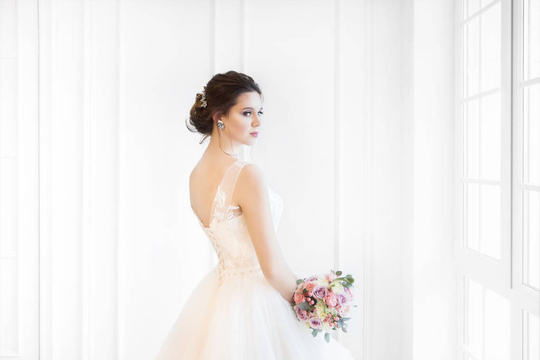 Beautiful brunette woman with bouquet posing in a wedding dress  - Фото, изображение