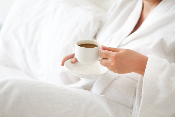 Woman wearing white robe with cup of coffee in her hands - Foto, afbeelding