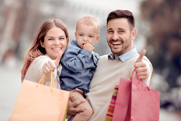 Retrato de mãe feliz, pai e filho com sacos de compras, mostrando os polegares para cima
. - Foto, Imagem
