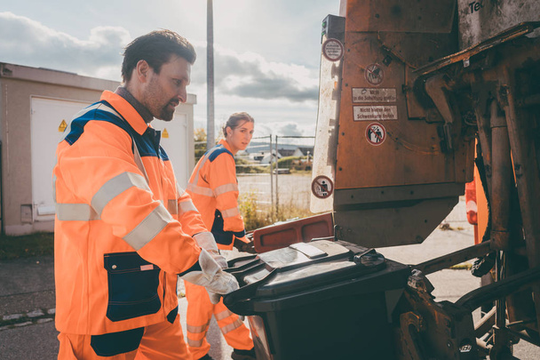 Müllmann und -frau reinigen Mülltonnen in Müllwagen und reinigen Straße - Foto, Bild