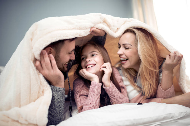 Μαμά, μπαμπάς και κόρη που βρίσκεται κάτω από την κουβέρτα, βλέποντας την ταινία και έχοντας υπέροχη στιγμή. - Φωτογραφία, εικόνα