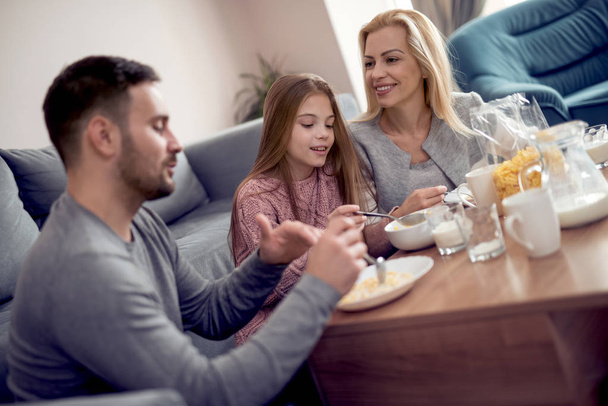 Family, food and people concept-happy mother, father and daughter having breakfast at home
. - Фото, изображение