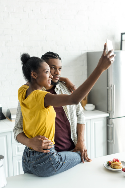smiling african american couple taking selfie with smartphone at kitchen - Fotoğraf, Görsel